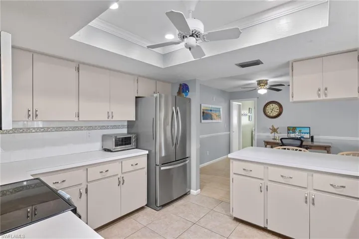 Kitchen featuring stainless steel fridge, a tray ceiling, tasteful backsplash, ceiling fan, and light tile floors