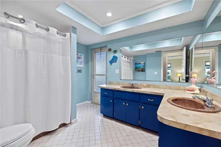 Bathroom featuring dual sinks, toilet, a tray ceiling, tile flooring, and large vanity