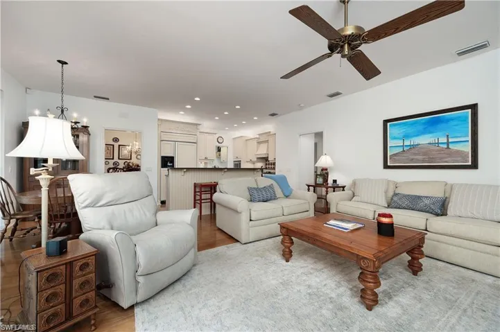 Living area featuring light wood-type flooring, visible vents, recessed lighting, and ceiling fan with notable chandelier