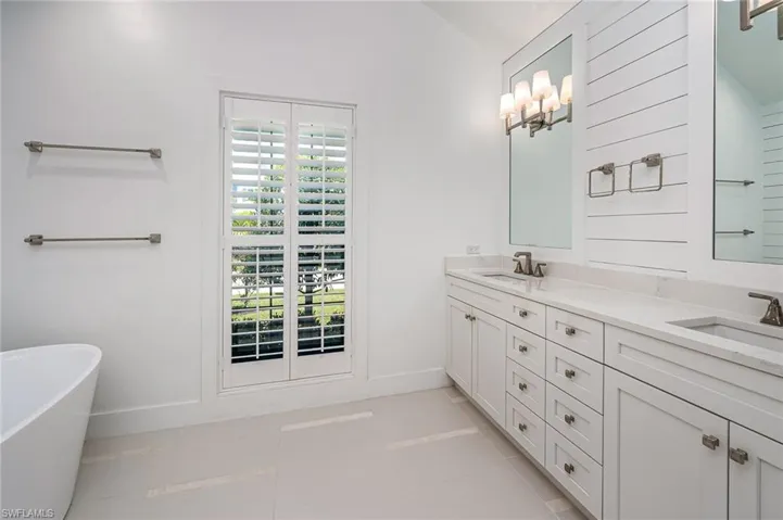 Full bath with tile patterned floors, a sink, double vanity, baseboards, and a soaking tub