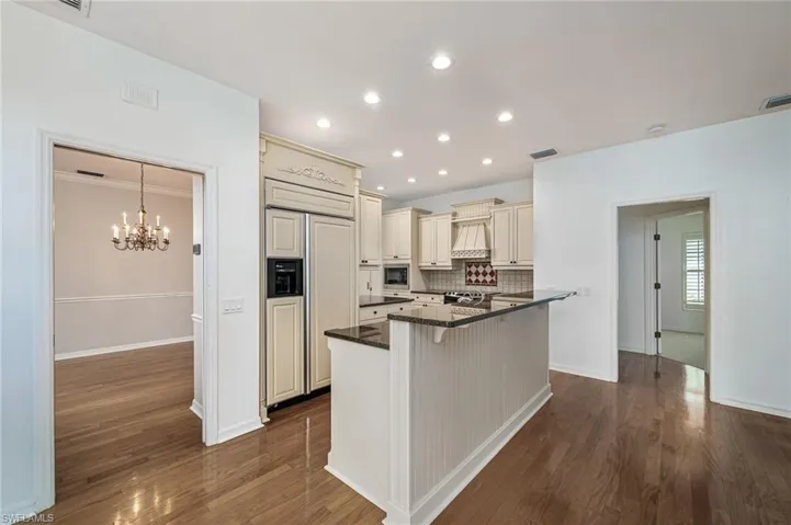 Kitchen with wood flooring, built in custom appliances, a kitchen bar with sink lots of cabinets and opening into the family room