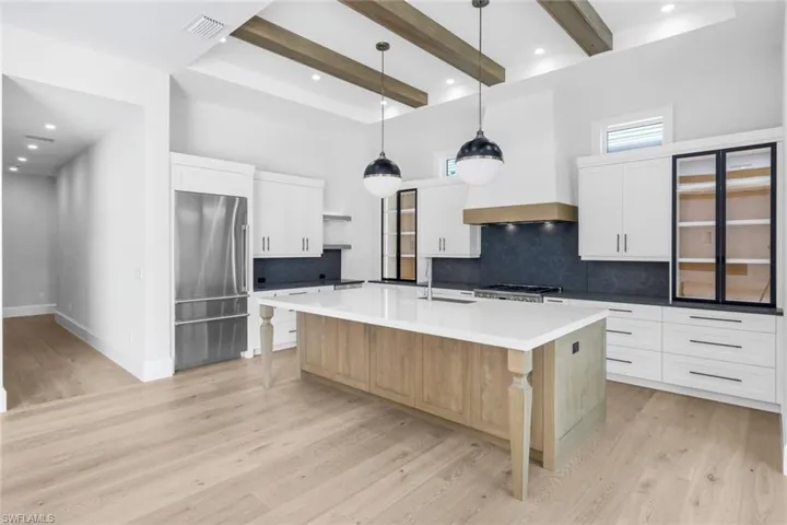 Two tone kitchen featuring two tone color scheme, high quality fridge, pendant lighting, decorative backsplash, and a large island with sink