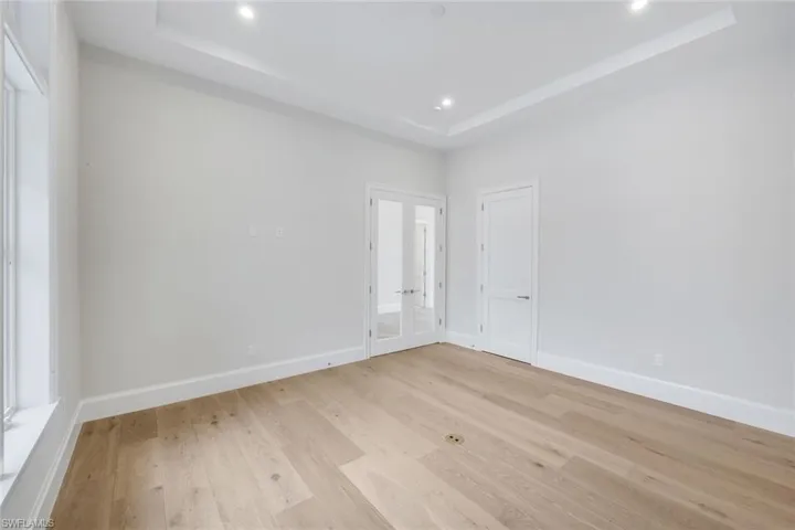 Unfurnished bedroom featuring a tray ceiling, french doors, light wood-style floors, and recessed lighting