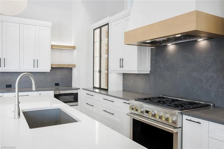 Kitchen featuring stainless steel appliances, white cabinets, tasteful backsplash, open shelves, and dark stone counters
