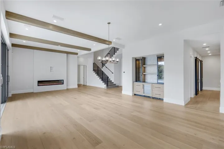Unfurnished living room with recessed lighting, beamed ceiling, light wood finished floors, and a glass covered fireplace