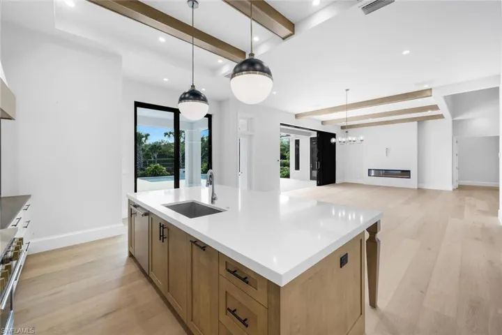 Kitchen with beam ceiling, light wood-type flooring, a kitchen island with sink, stainless steel range, and light stone counters