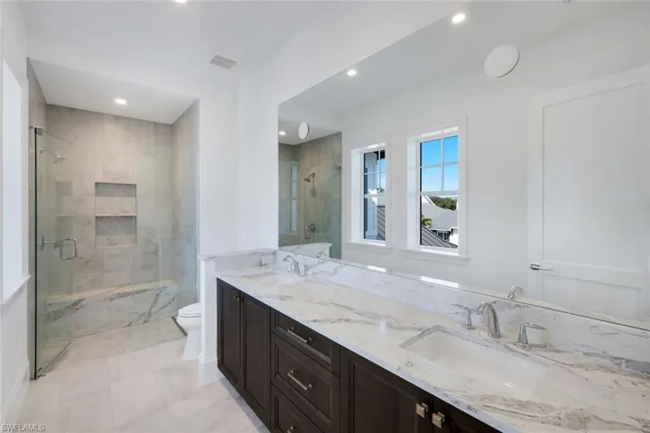 Full bath featuring a marble finish shower, double vanity, and recessed lighting