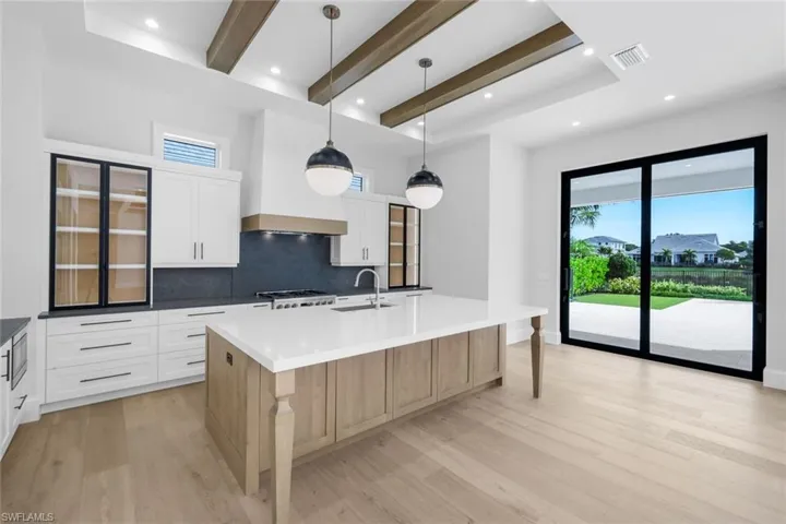 Two tone kitchen featuring beam ceiling, dual tone cabinetry, decorative light fixtures, a spacious island, and tasteful backsplash