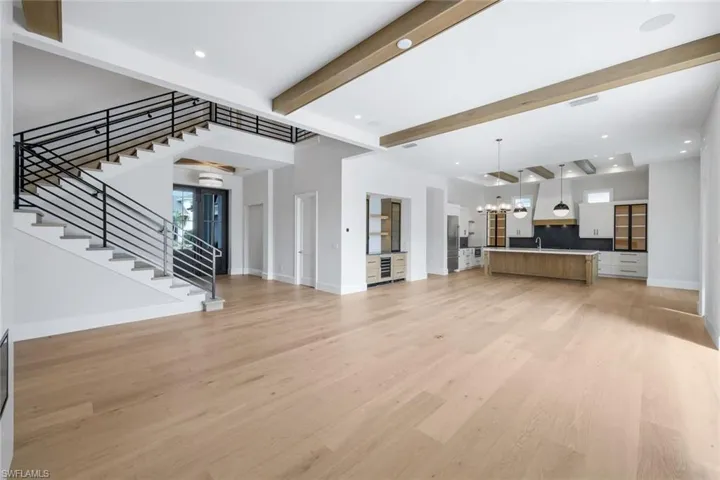 Unfurnished living room featuring beamed ceiling, a chandelier, light wood-type flooring, and wine cooler