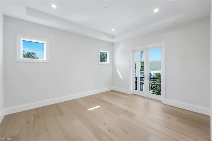 Empty room featuring light wood-type flooring, french doors, recessed lighting, and a tray ceiling