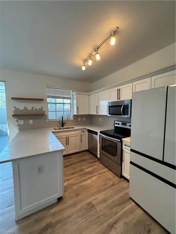 Kitchen with stove, refrigerator, kitchen peninsula, hardwood / wood-style flooring, and white cabinetry