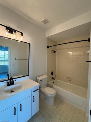Full bathroom with tile patterned flooring, vanity, tiled shower / bath combo, and toilet
