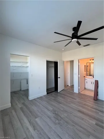 Unfurnished bedroom featuring ensuite bathroom, a walk in closet, ceiling fan, light hardwood / wood-style floors, and a closet