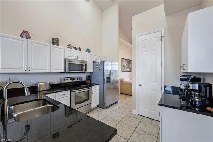 Kitchen with sink, white cabinetry, appliances with stainless steel finishes, dark stone countertops, and a towering ceiling