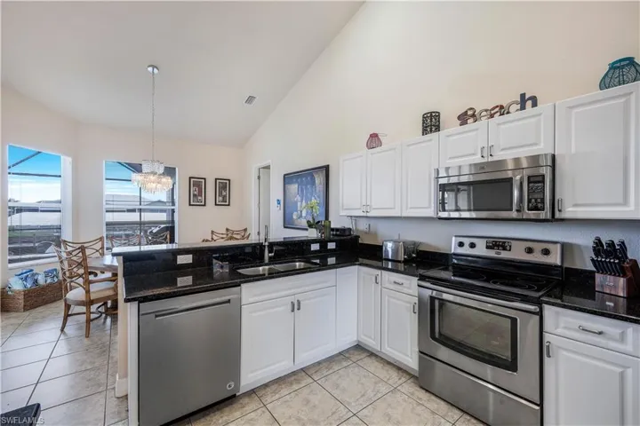 Kitchen featuring appliances with stainless steel finishes, white cabinetry, kitchen peninsula, sink, and a notable chandelier