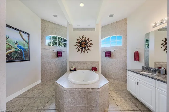 Bathroom with tile walls, a wealth of natural light, tiled bath, and vanity