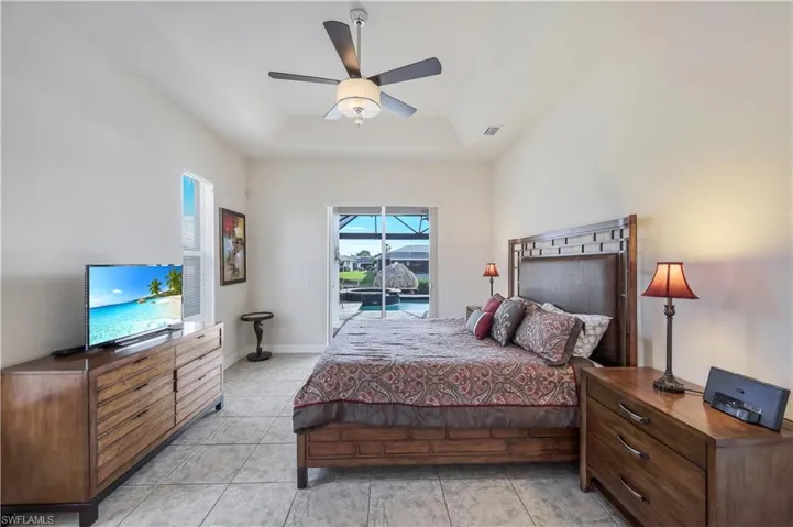 Tiled bedroom featuring ceiling fan, a raised ceiling, and access to exterior