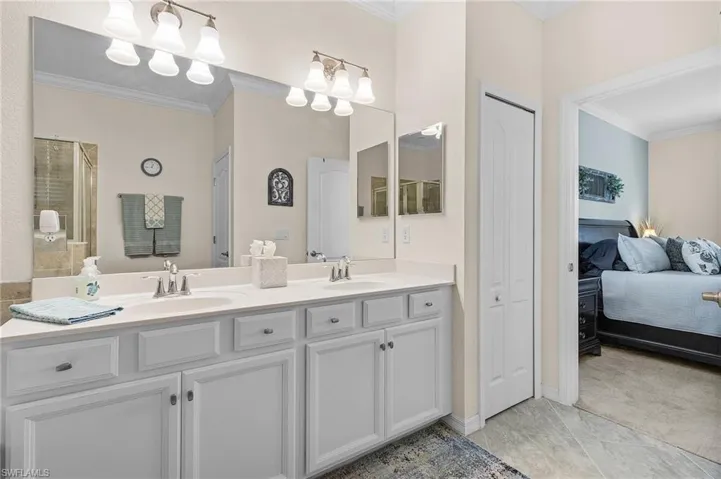 Bathroom featuring tile patterned floors, double vanity, crown molding, and an inviting chandelier