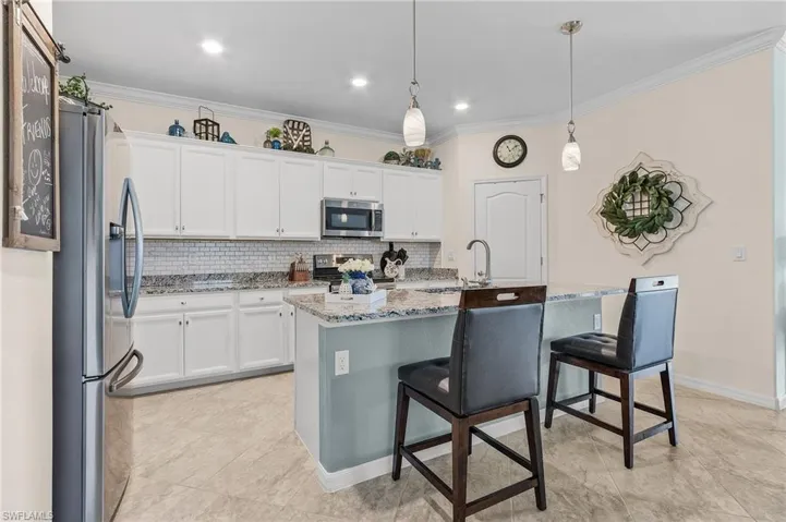 Kitchen featuring appliances with stainless steel finishes, light stone countertops, an island with sink, backsplash, and sink