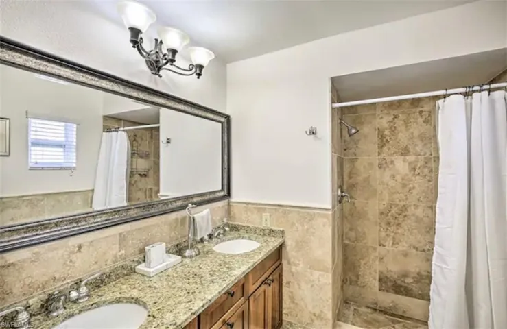 Bathroom featuring double vanity, a shower stall, a wainscoted wall, tile walls, and hanging lights