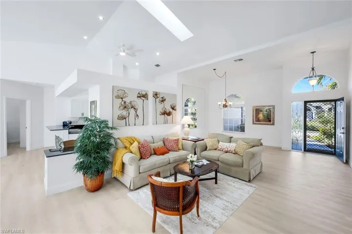 Living room featuring vaulted ceiling, a skylight, light wood finished floors, a ceiling fan, and hanging lights