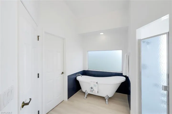 Bathroom featuring light wood-style floors, a wainscoted wall, a freestanding tub, and a stall shower