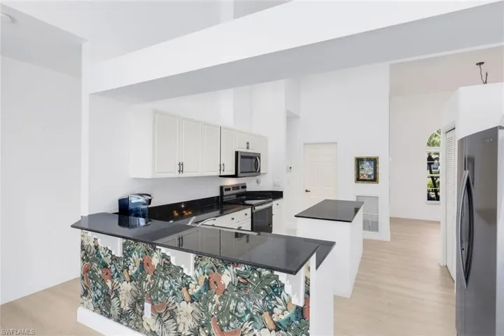Kitchen with a kitchen island, stainless steel appliances, dark stone countertops, light wood-style flooring, and white cabinets
