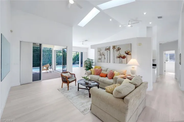 Living room featuring light wood finished floors, a skylight, a ceiling fan, and lofted ceiling