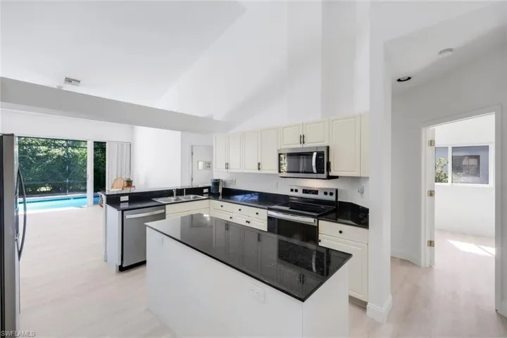Kitchen with stainless steel appliances, light wood-style floors, a peninsula, a center island, and dark stone counters