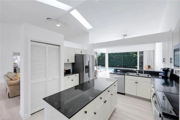 Kitchen featuring a skylight, light wood-type flooring, white cabinetry, stainless steel appliances, and dark stone countertops
