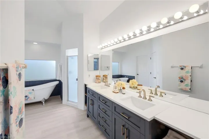 Full bath featuring a freestanding tub, double vanity, light wood-style flooring, and a stall shower