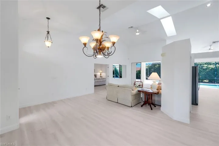 Living room featuring light wood finished floors, a skylight, vaulted ceiling, a ceiling fan, and suspended lighting