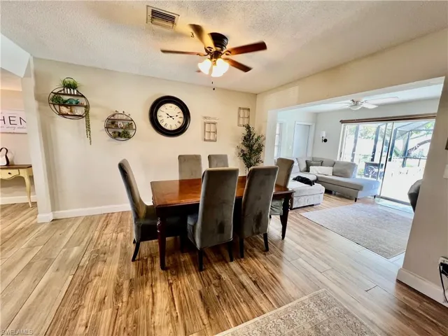Dining room with ceiling fan, a textured ceiling, and light  wood-style floors.