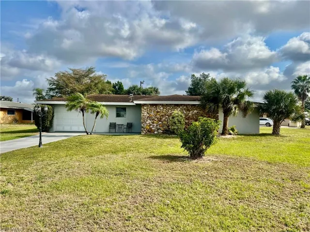 Single story home featuring a garage and a front lawn nicely landscaped with palms etc.