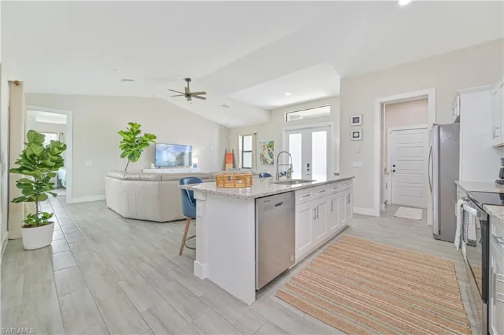 Kitchen featuring ceiling fan, stainless steel appliances, a center island with sink, sink, and white cabinets