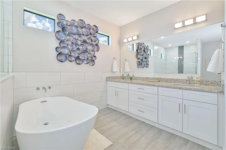 Bathroom with tile walls, a bathing tub, dual sinks, tile flooring, and large vanity