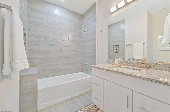 Bathroom with tile floors, tiled shower / bath combo, and large vanity