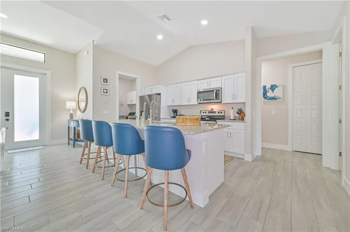 Kitchen featuring an island with sink, stainless steel appliances, vaulted ceiling, light stone counters, and white cabinets