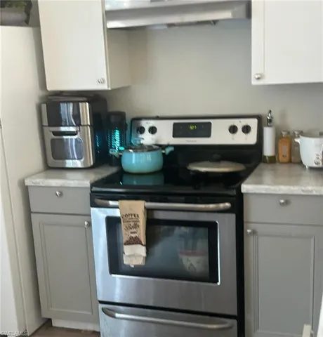 Kitchen featuring electric range, freestanding refrigerator, gray cabinets, light countertops, and exhaust hood