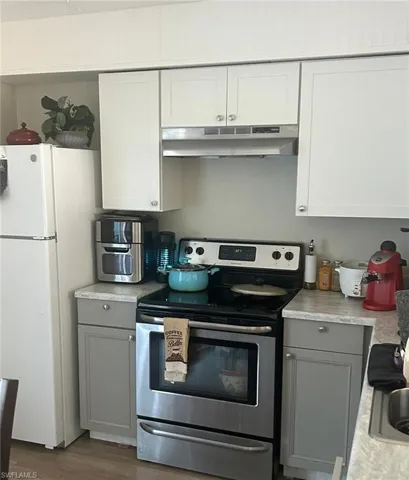 Kitchen with gray cabinetry, under cabinet range hood, light countertops, freestanding refrigerator, and stainless steel range with electric stovetop