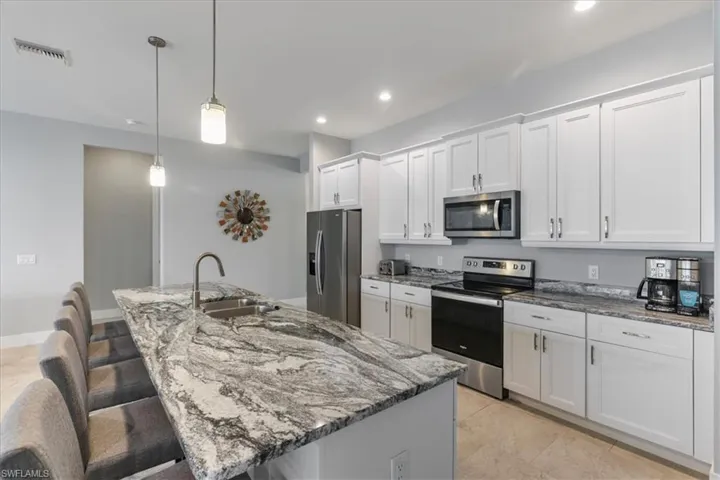 Kitchen with light stone countertops, stainless steel appliances, a kitchen breakfast bar, pendant lighting, and white cabinets