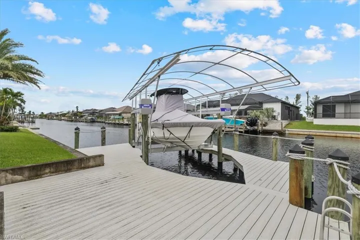 Dock featuring boat lift, a water view, a residential view, and a lawn