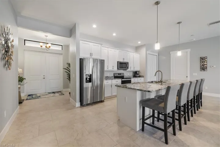Kitchen featuring stainless steel appliances, a kitchen breakfast bar, dark stone countertops, an island with sink, and white cabinetry