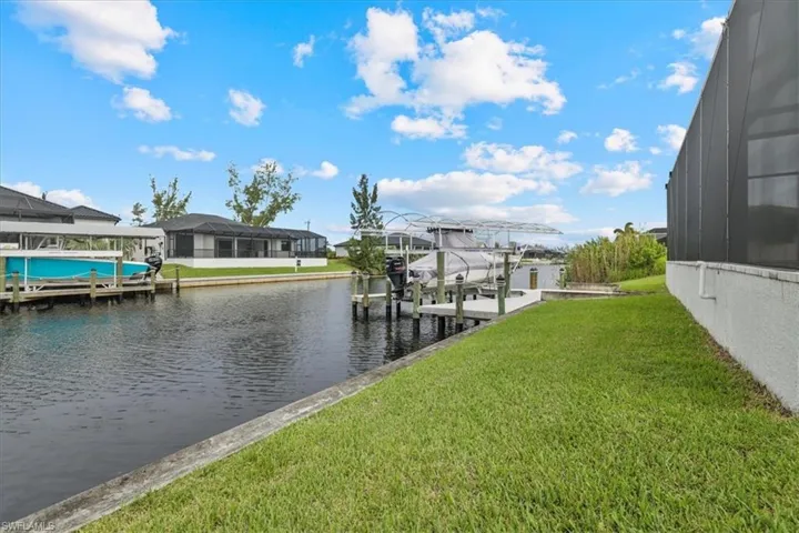 Dock featuring boat lift, a lawn, glass enclosure, and a water view