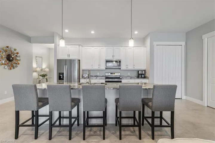Kitchen with white cabinetry, appliances with stainless steel finishes, light stone countertops, decorative light fixtures, and recessed lighting