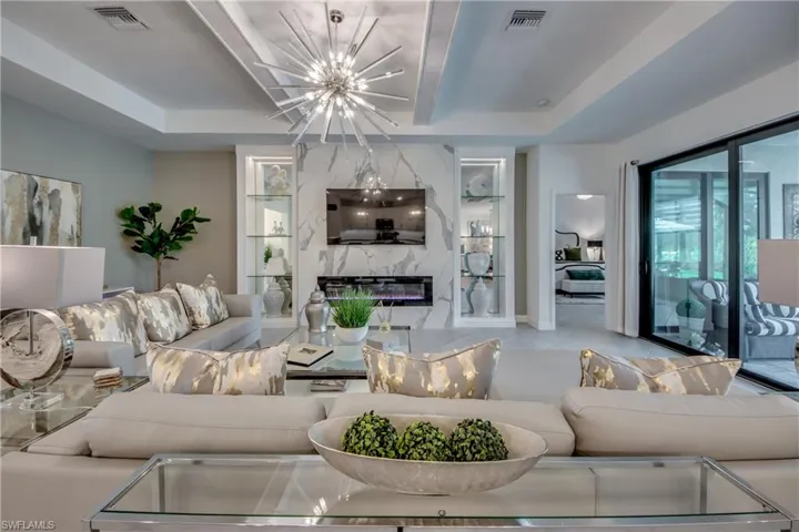 Living room featuring a raised ceiling, a high end fireplace, light tile patterned flooring, and a notable chandelier