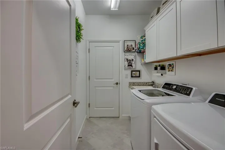 Laundry area with light tile patterned flooring, cabinets, washing machine and dryer, and sink