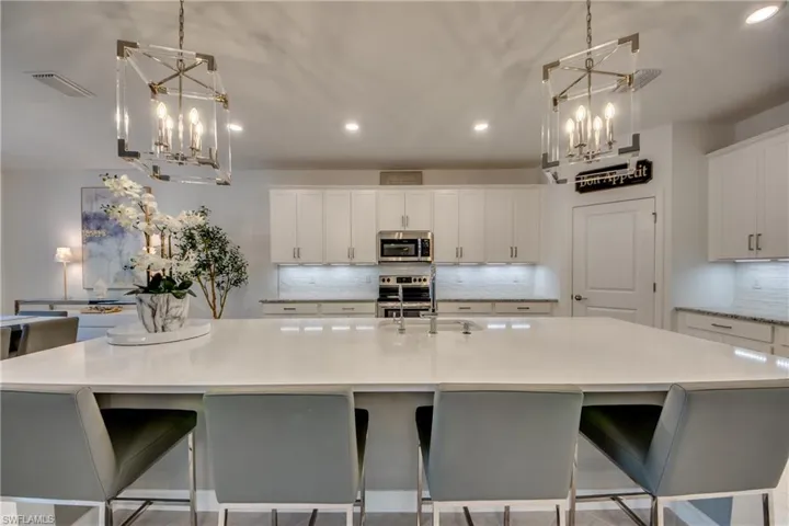 Kitchen featuring a breakfast bar area, stainless steel appliances, pendant lighting, white cabinetry, and a large island with sink