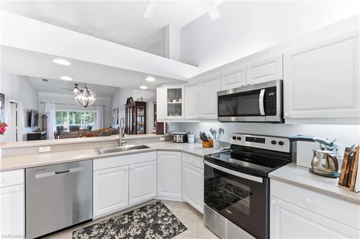 Kitchen with stainless steel appliances, white cabinets, vaulted ceiling, hanging lights, and glass fronted cabinets