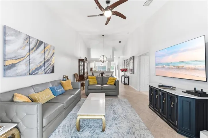 Living room with ceiling fan, light tile patterned floors, and lofted ceiling